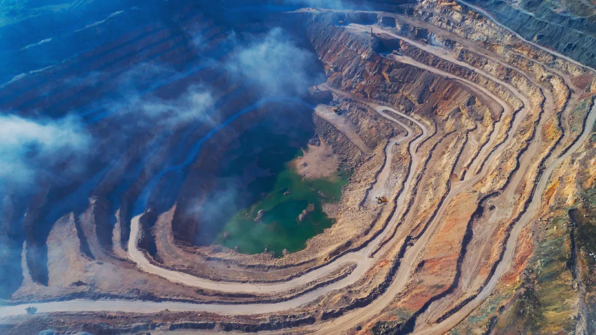 Aerial view of a large open-pit mine with terraced layers and smoke or fog.