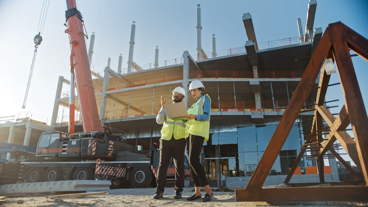 Two construction workers with plans in front of a construction site.