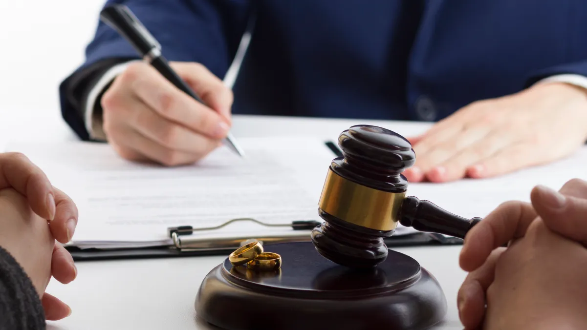 Person signing document near a judge's gavel on a desk, suggesting a legal setting.