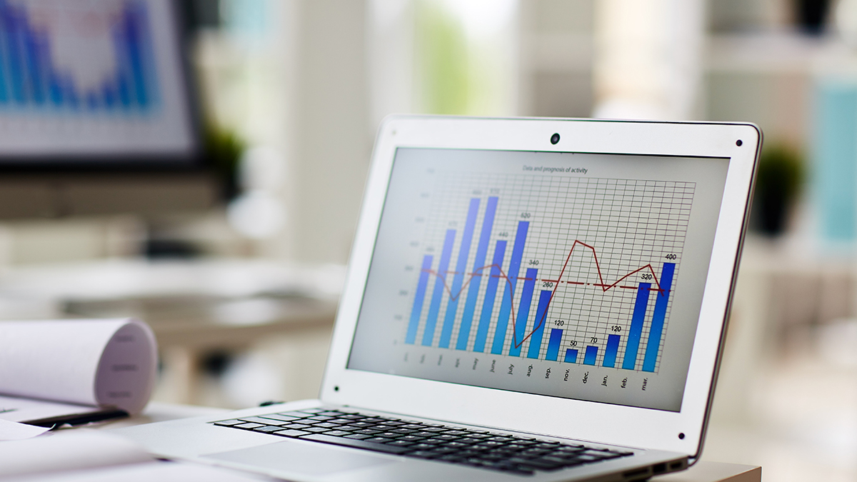 Laptop on a desk displaying a colorful bar and line graph chart, in a bright office setting.