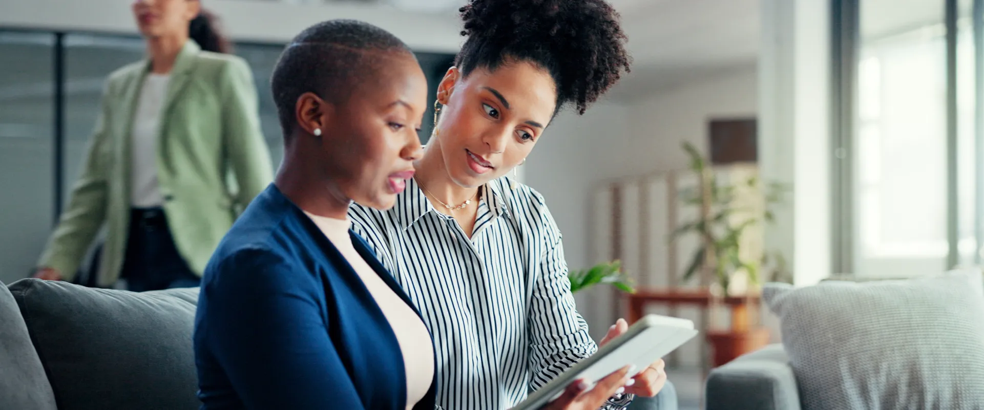 Two people in business attire holding a tablet in a modern office setting.