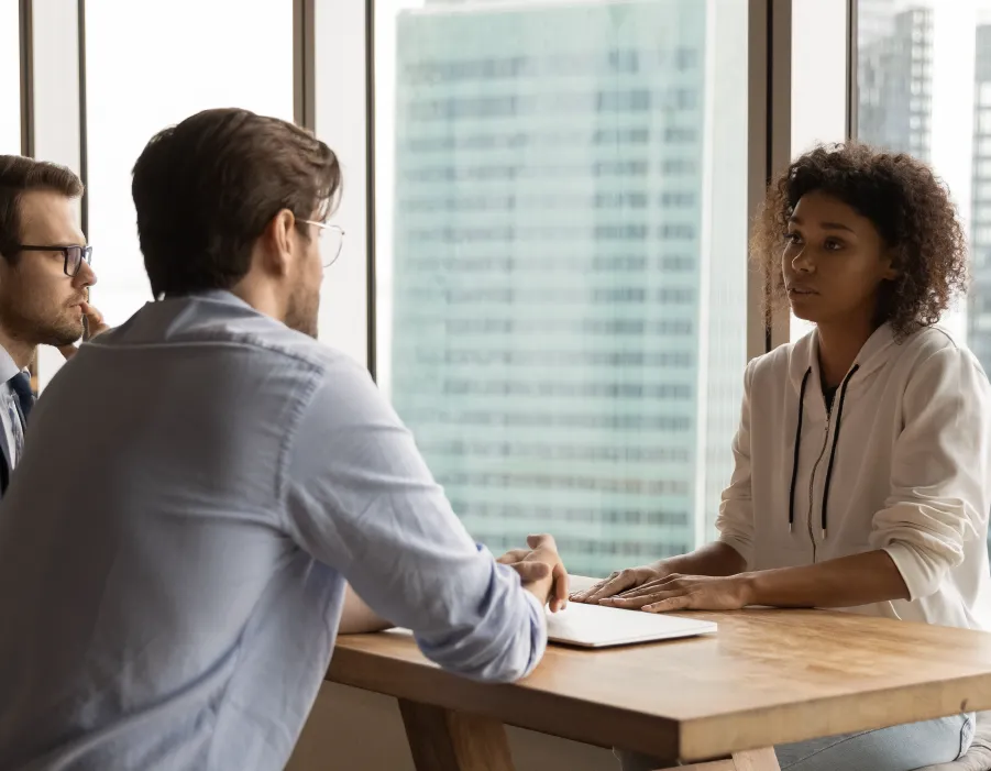 Three individuals in a meeting, one noting down details, with cityscape in the background.